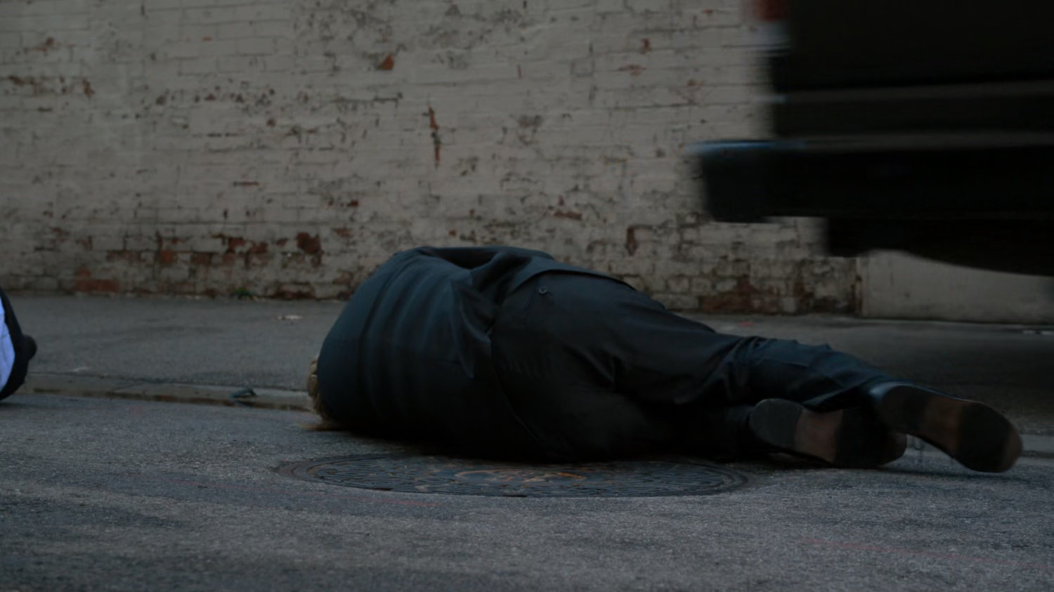 Body laying on manhole cover in alley.