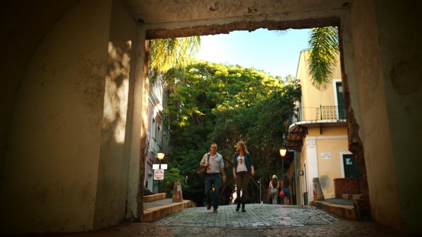 Bobbi and Coulson walk on cobblestone street outside stone wall in San Juan.