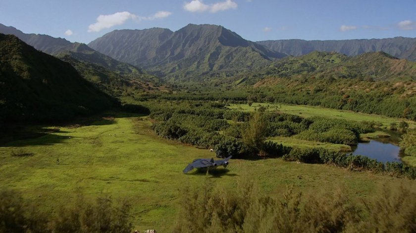 Aerial of tropical fields and mountains, with a quinjet.