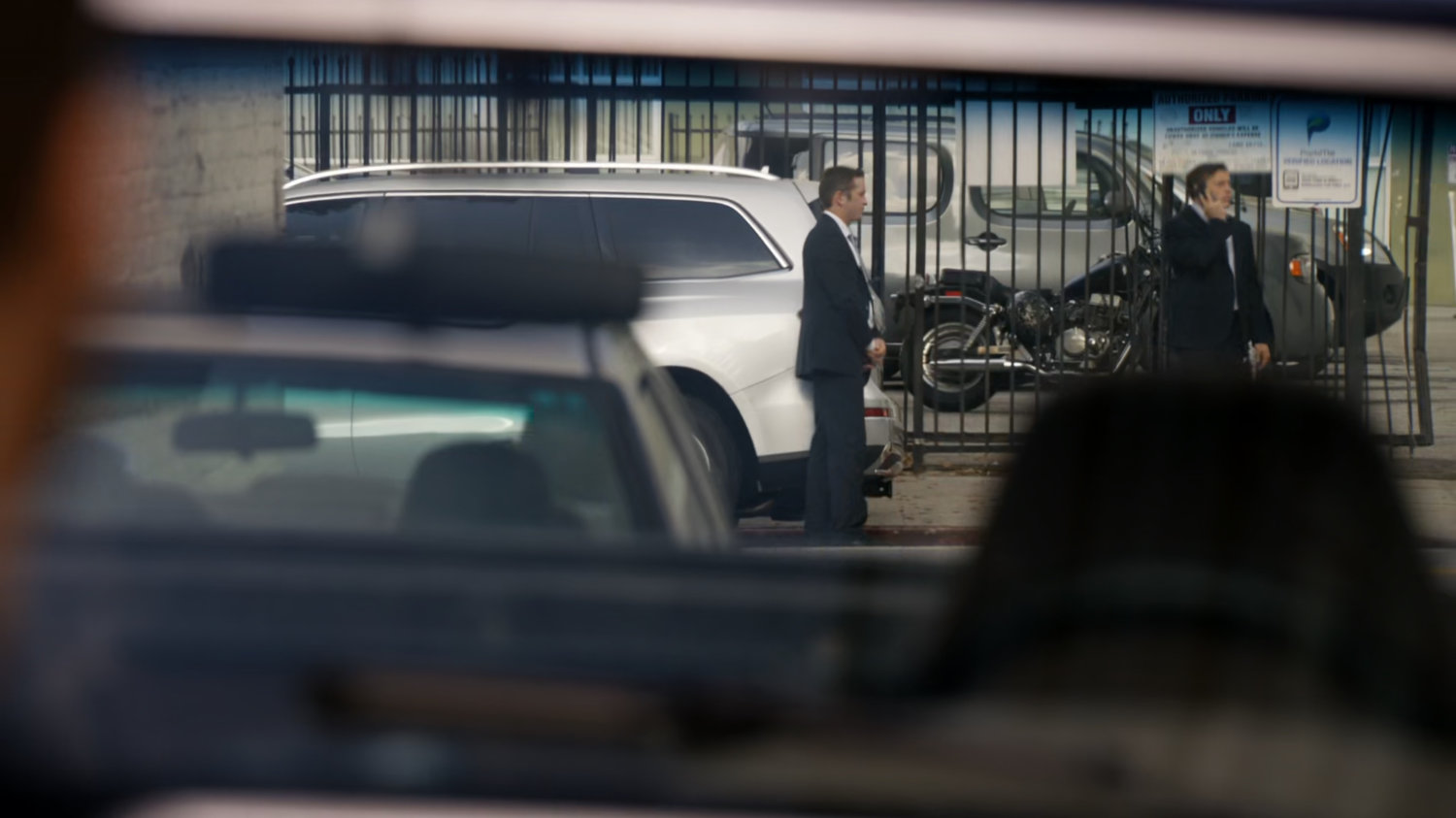 Two men in suits stand outside a fence by a Vancouver street.