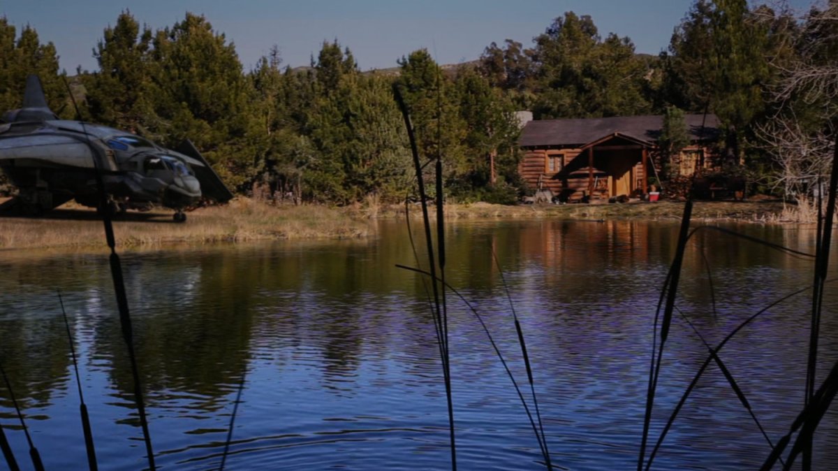 Exterior of Nick Fury's cabin by a lake, with a quinjet parked nearby.