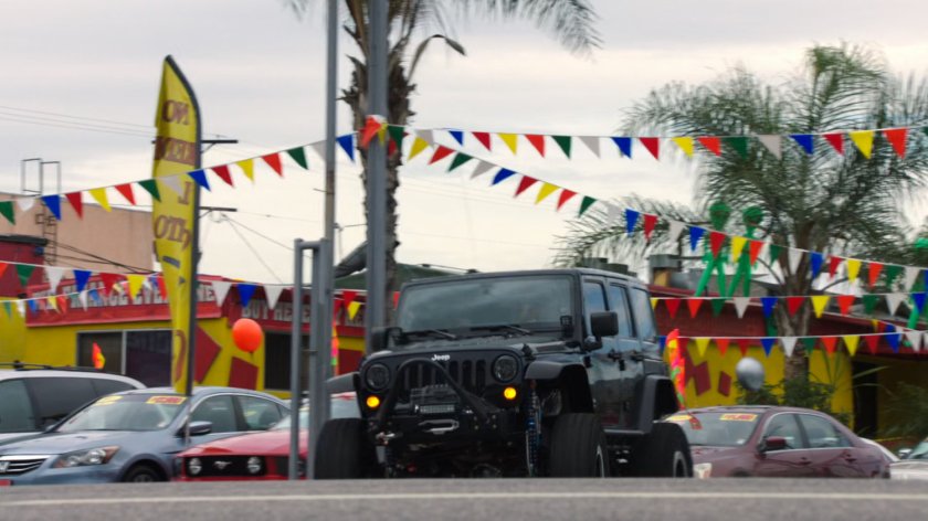 A black jeep drives off the used car lot.