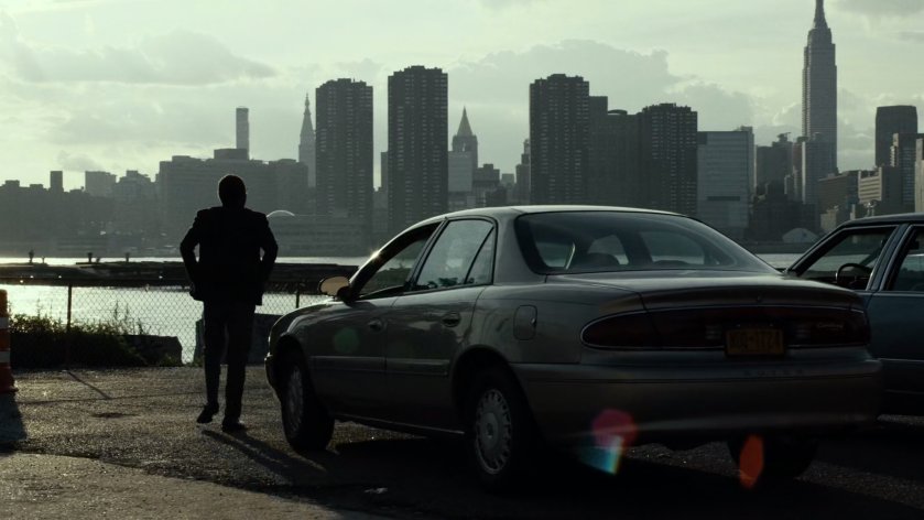 Man exits car by East River with New York City in background.