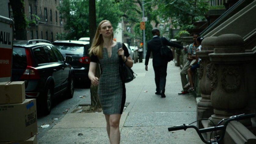 Karen walks along sidewalk by brownstones.