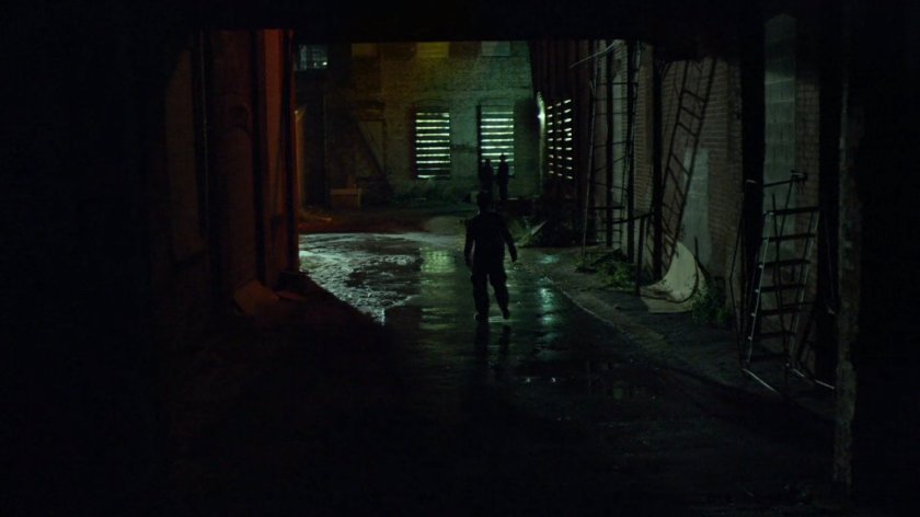 Blind man walks down alley outside Russian warehouse.