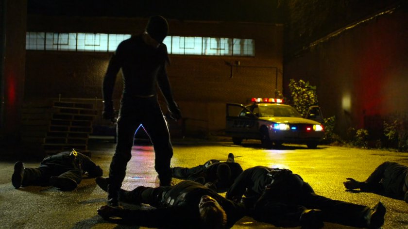 Daredevil standing over downed police officers in pallet yard outside Russian warehouse.
