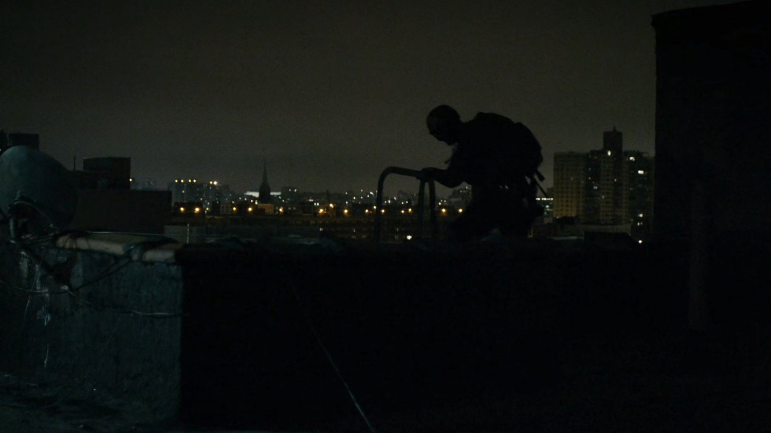 Silhouetted sniper sets up on rooftop.