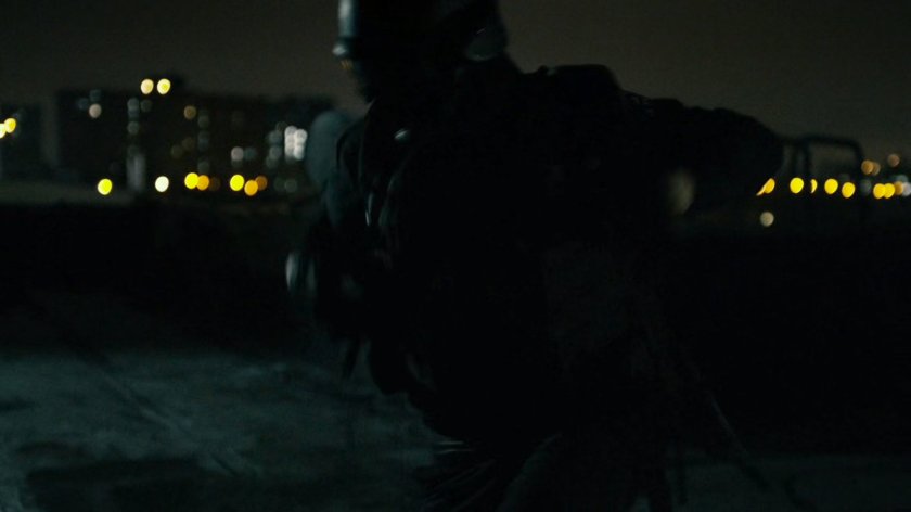 Silhouetted sniper sets up on rooftop.