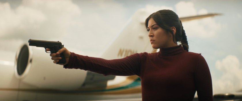 Maya holding gun with airplane in background.