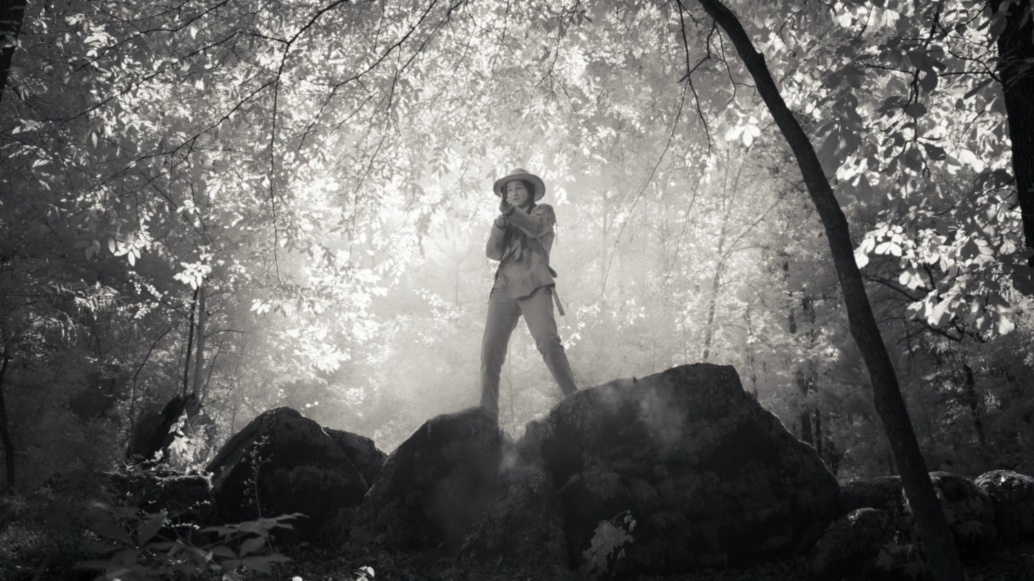 Tuklo with rifle on boulders in woods.