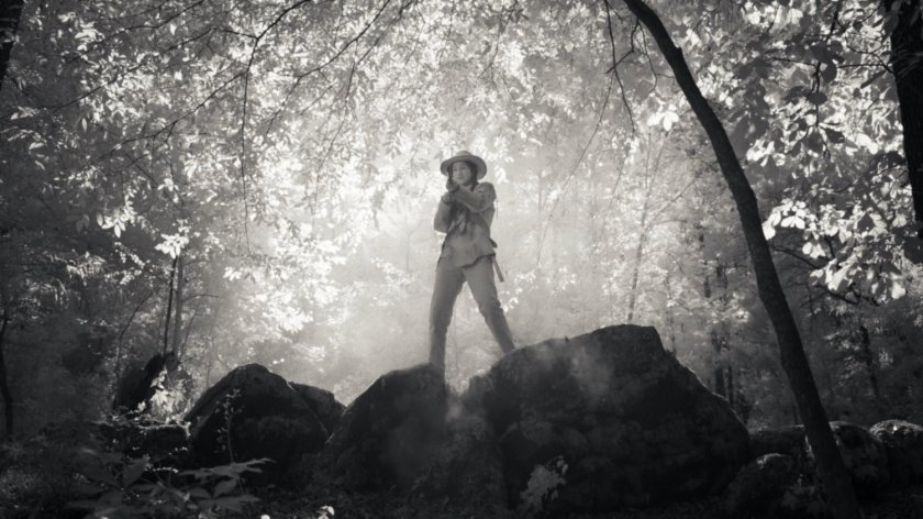 Tuklo with rifle on boulders in woods.