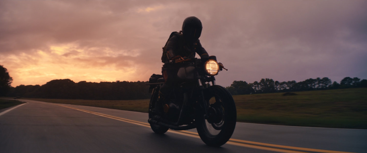 Maya on her motorcycle on a country road at sunset.
