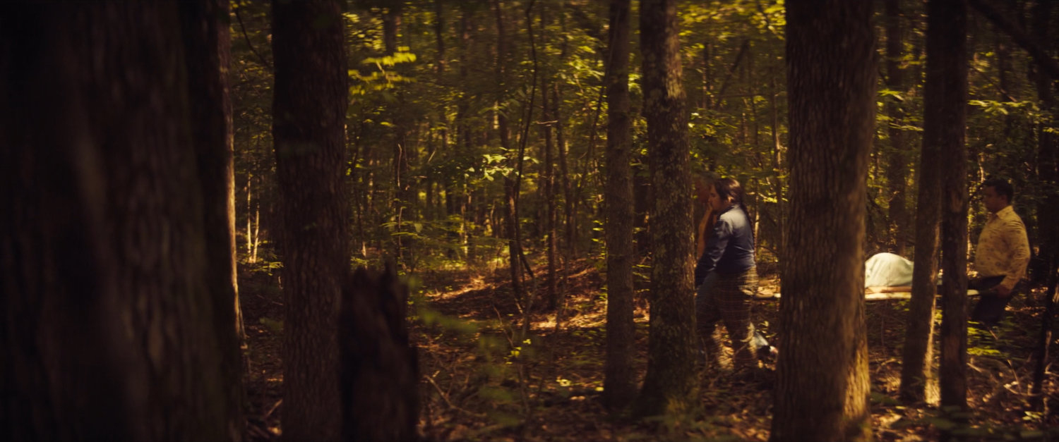 Women carrying stretcher through woods.