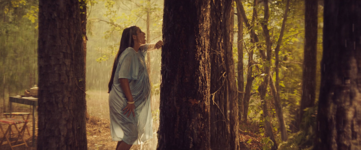 Young Chula standing in rain in woods.