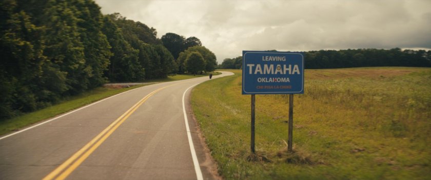 Maya on her motorcycle on a country road, with a sign reading "Leaving Tamaha, Oklahoma."