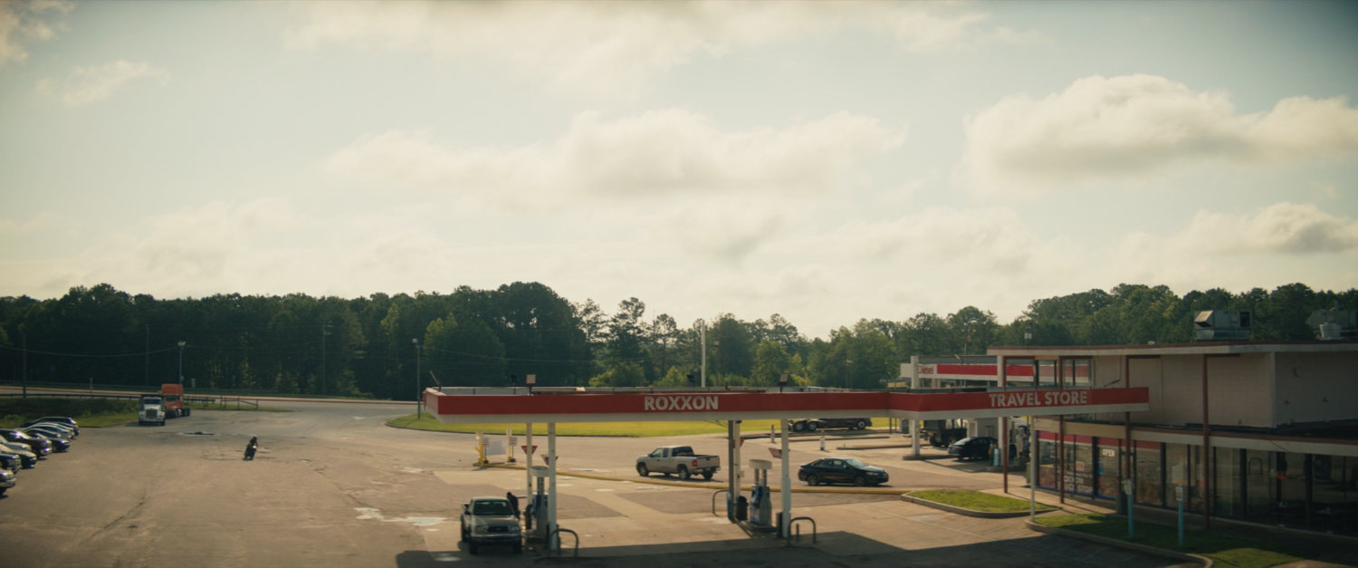 High angle view of Maya pulling her motorcycle in to Roxxon Travel Store.