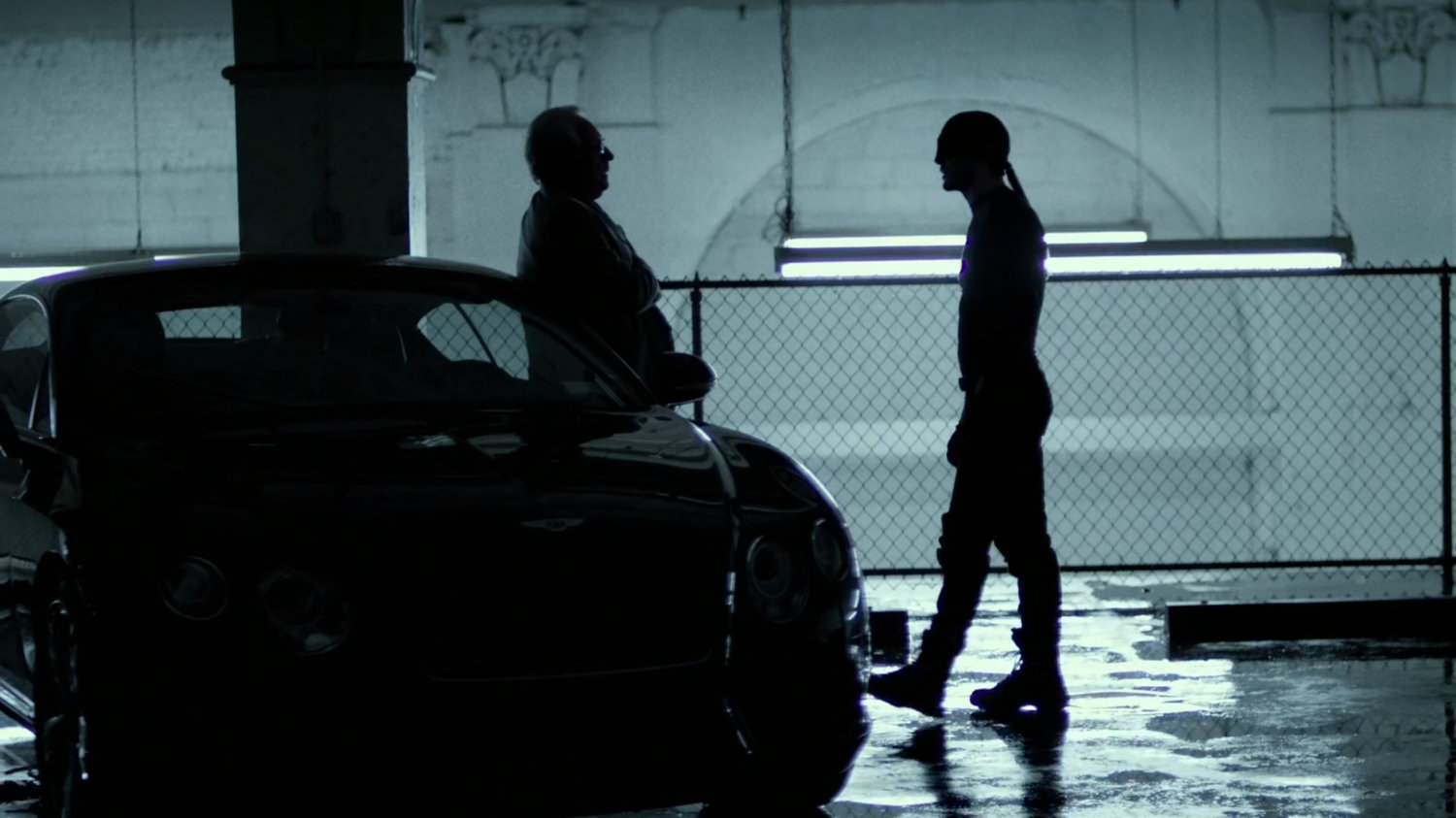 The man in black confronts Owlsley in stark white parking garage.