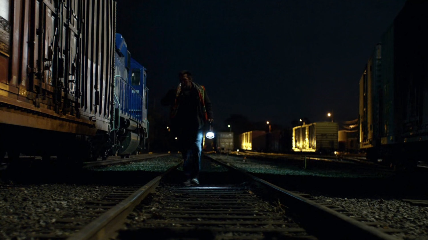 Man walking through railroad yard at night.