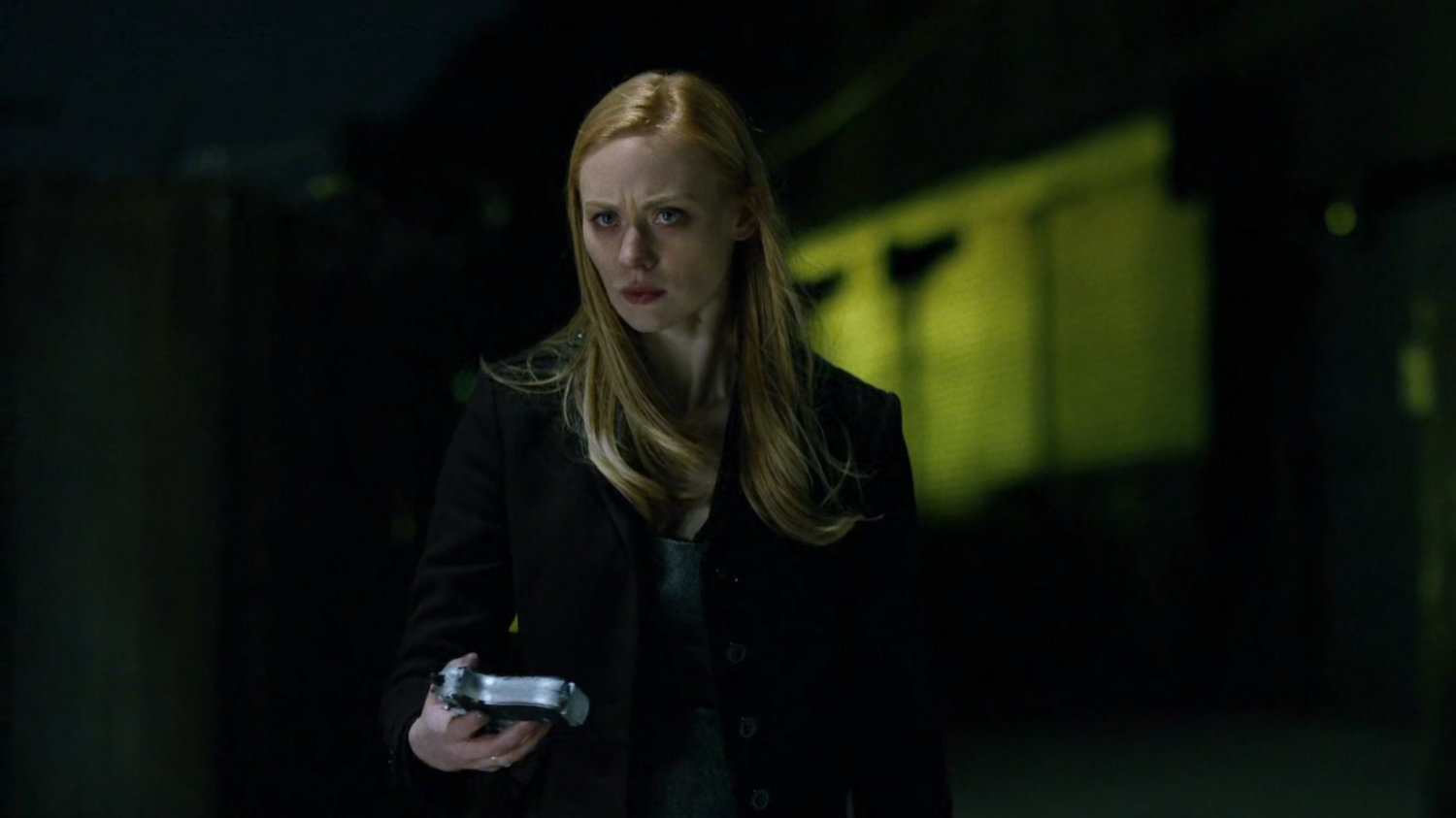 Karen standing at the water's edge with a gun at night.