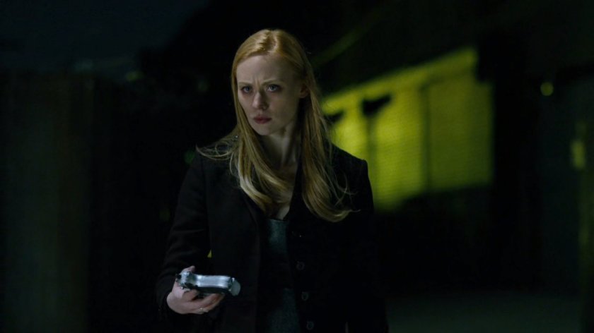 Karen standing at the water's edge with a gun at night.