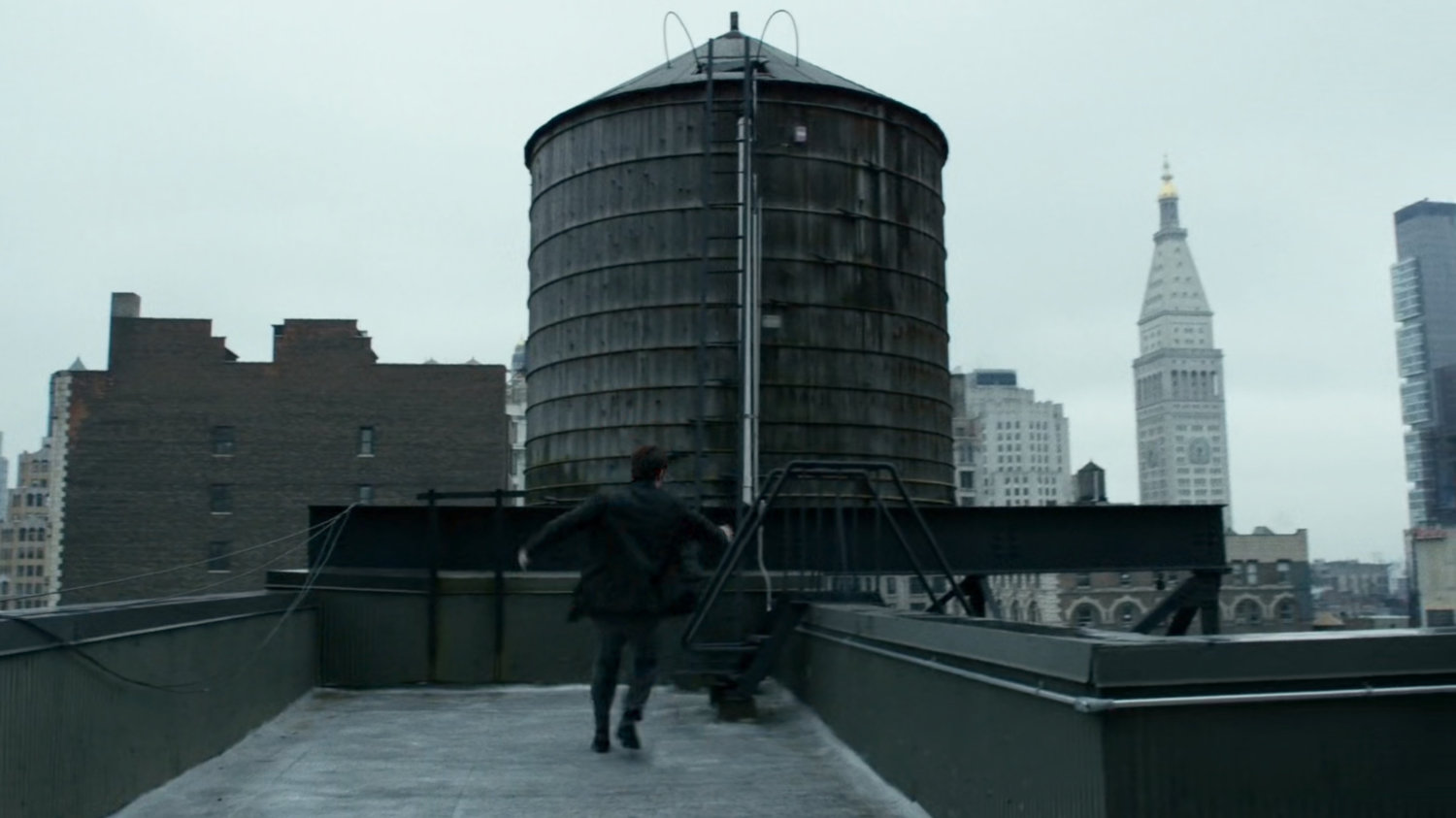 Matt runs across a New York rooftop, by a water tower.
