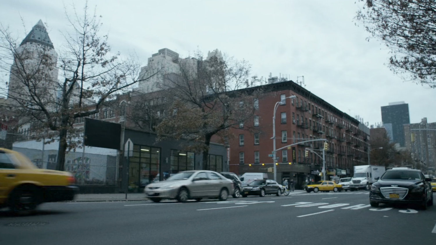 A black sedan drives past a New York street corner.
