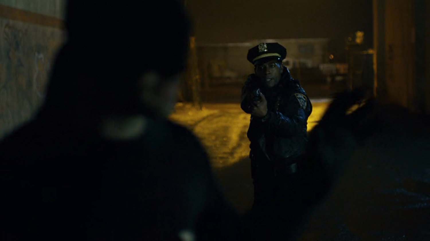 Officer Brett Mahoney draws gun on Man in Black in dark alley.