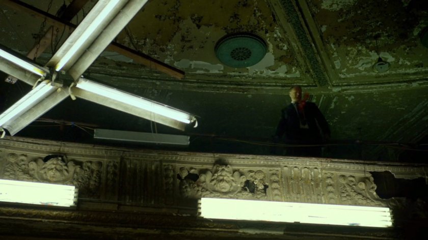 Man on balcony inside abandoned theater.