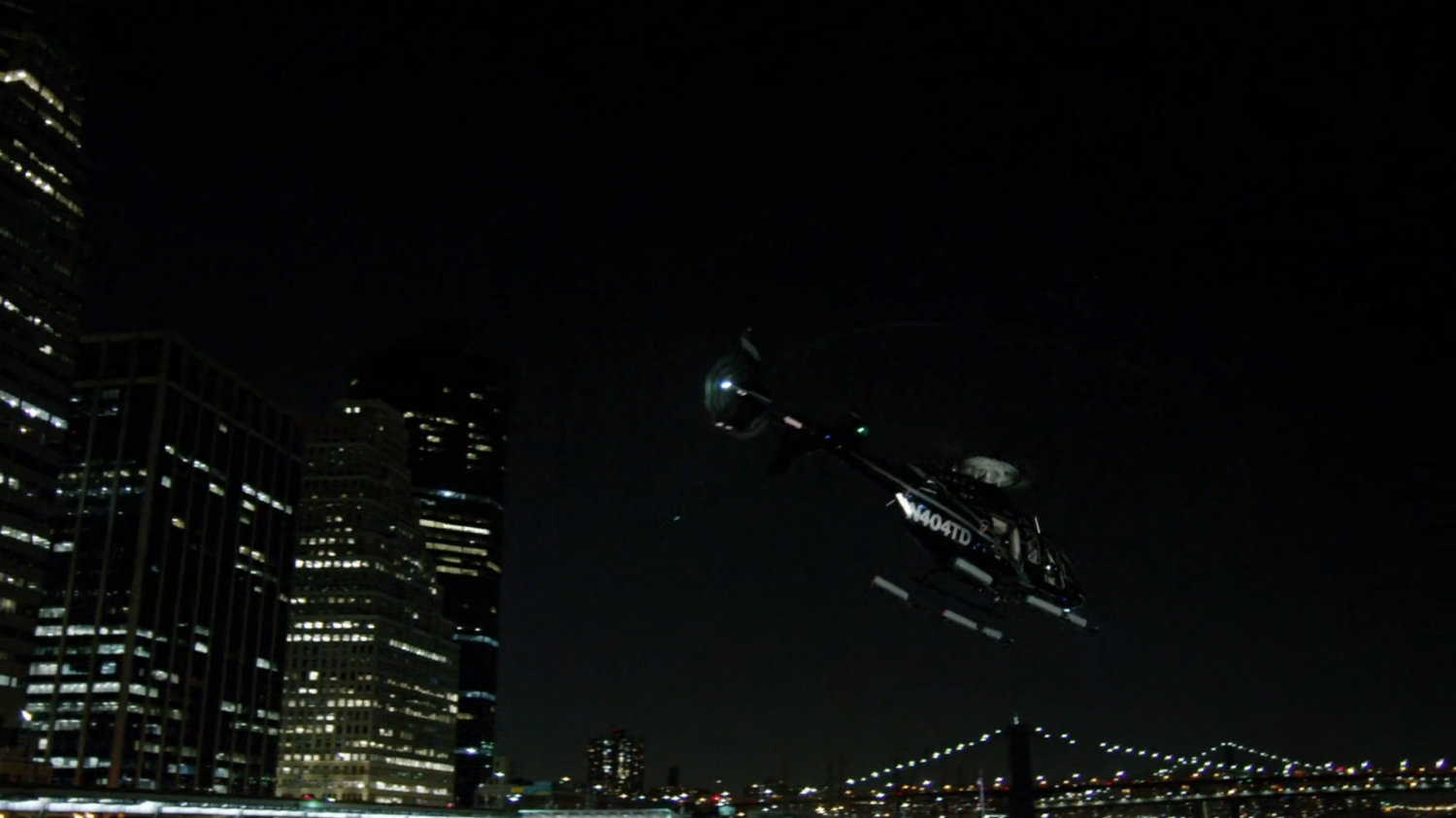 Helicopter departing heliport with bridges in background.