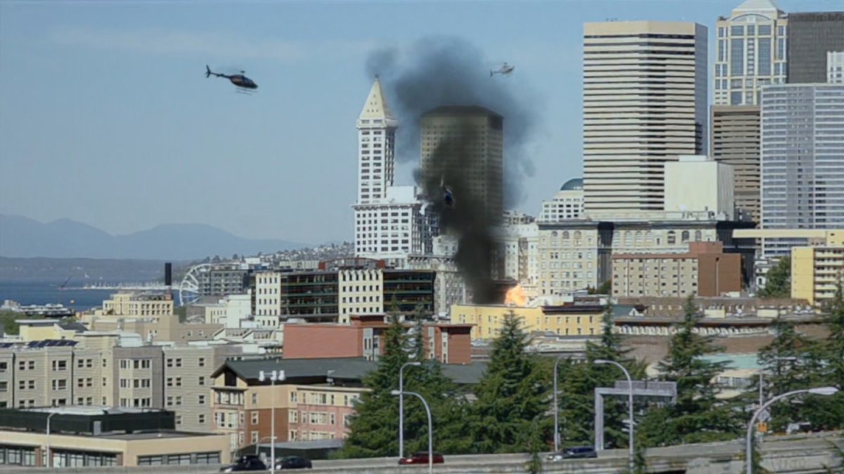 Helicopters over downtown Seattle which has smoke rising from it.