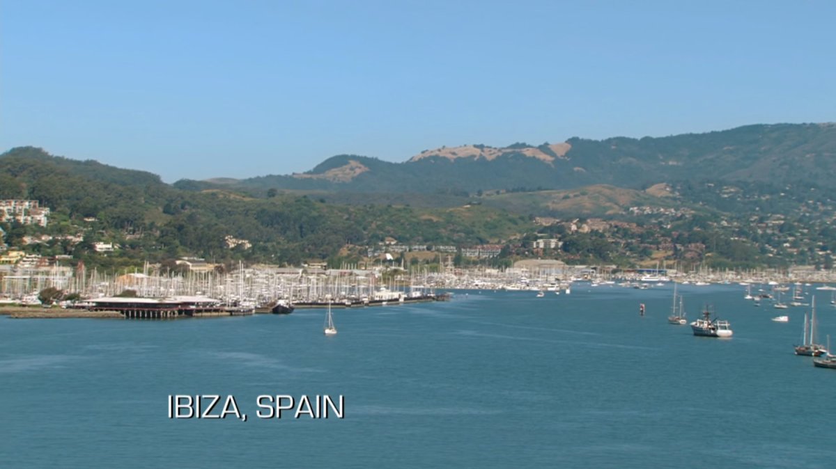 Aerial view of marina and hills. Text: Ibiza, Spain.