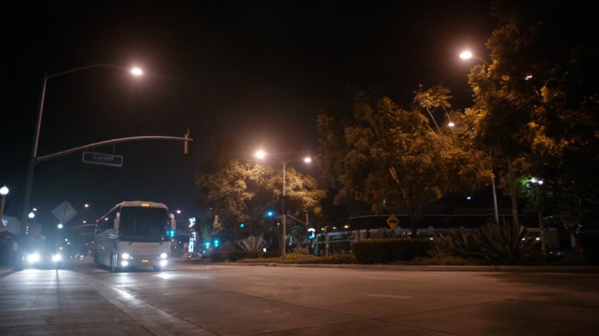 A bus approaches an intersection at nighttime.