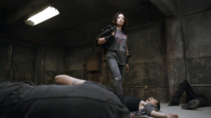 May standing over three unconscious men in a warehouse.