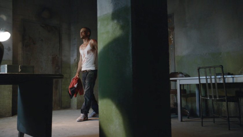 A bloody Hunter is escorted into a warehouse back room.