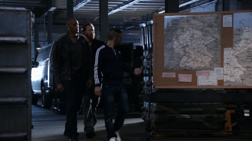 Kebo leads Hunter past maps in a HYDRA warehouse.