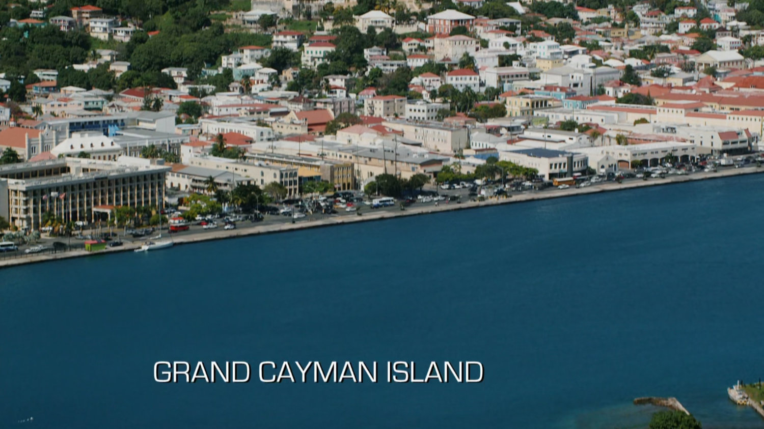 Aerial view of ocean and town. Text: Grand Cayman Island.