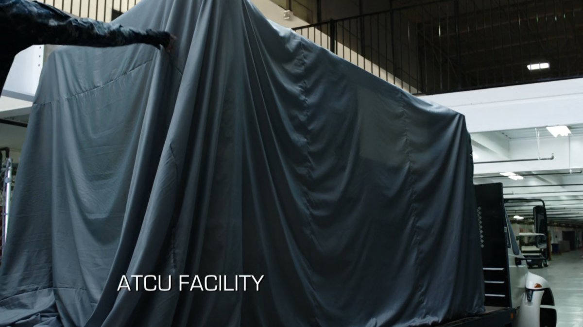 A shrouded containment box on the back of a truck in a warehouse. Text: ATCU Facility.