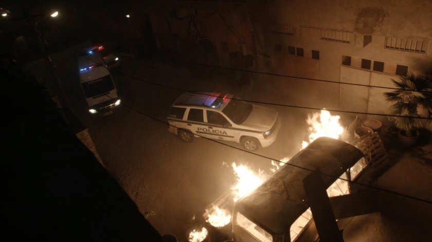 Police car and ambulance blocked by flaming wreckage on a Bogota street.