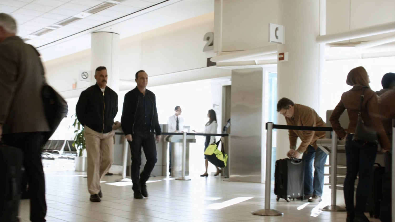 Coulson and Talbot walk through a busy airport.