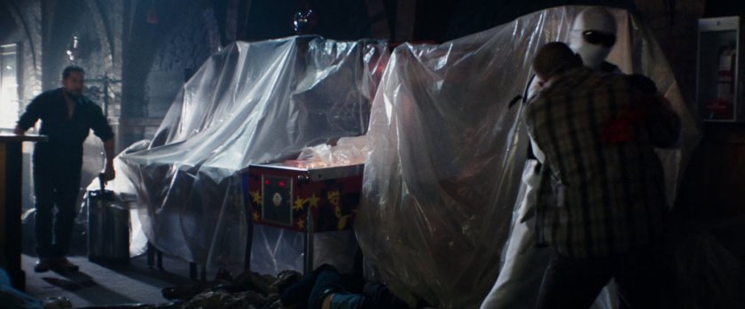 Wade beating someone up inside a bar in front of plastic covered pinball machines.