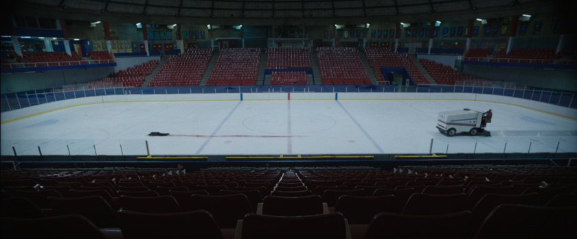 A Zamboni heading towards a man crawling on ice rink.
