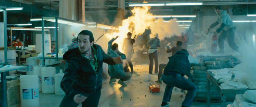 Man running through a drug warehouse while fire breaks out behind him.