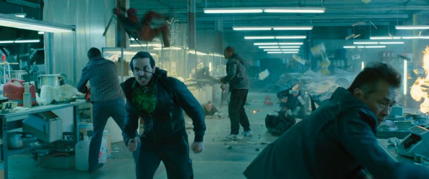 Man running through a drug warehouse as Deadpool kills people behind him.