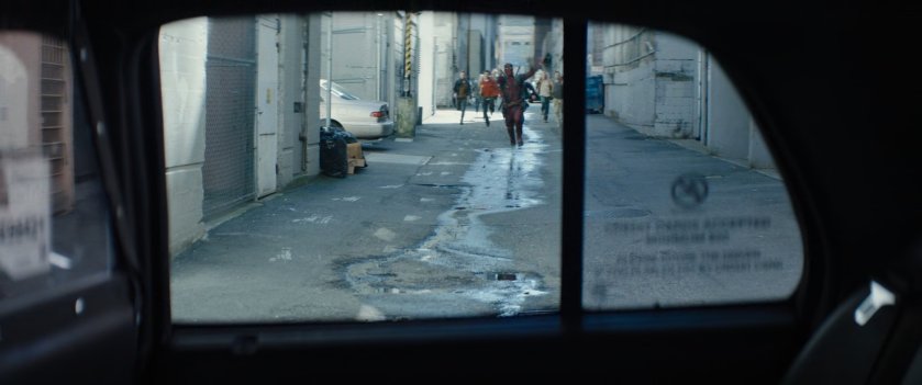 Deadpool running through alley toward taxi cab followed by a crowd of people.