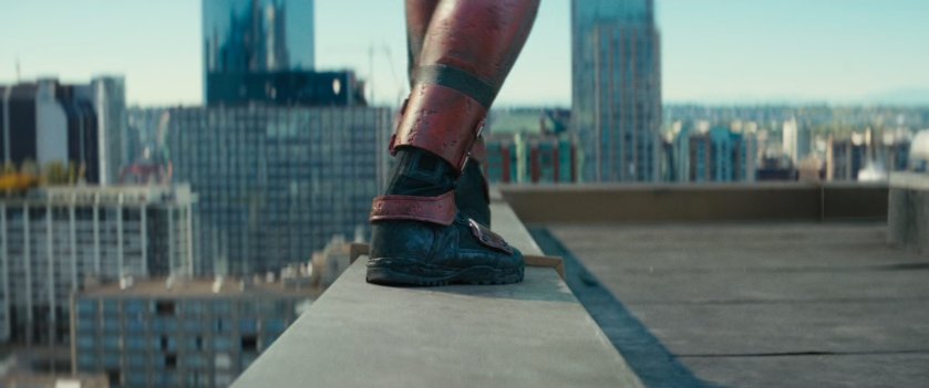 Close-up of Deadpool's feet on building ledge, with high rises in background.