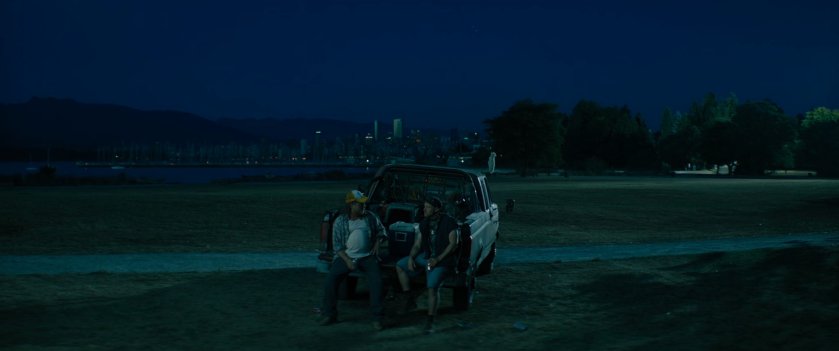 Two men sitting in the back of a pickup truck in a field.