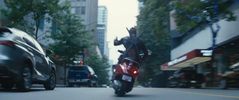Deadpool on red scooter following convoy truck.