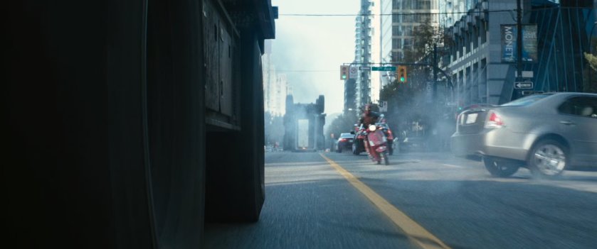 Deadpool on red scooter following convoy truck.
