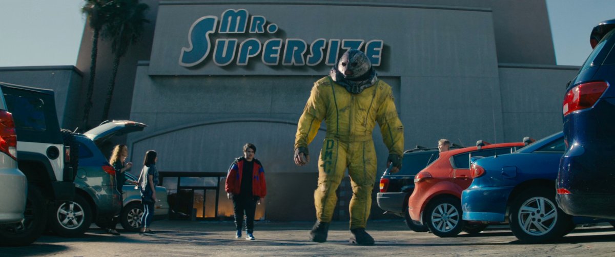 Russell and Juggernaut walking through parking lot of Mr. Supersize store.