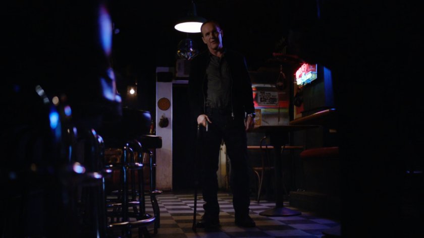 Coulson standing in a dark bar.